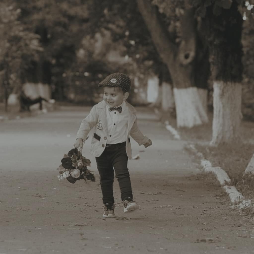 foto em preto e branco de menino trajado como nos anos 20 segurando um ramalhete num caminho arborizado