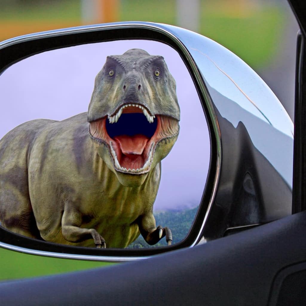 foto de retrovisor de carro com a figura de um dinossauro de frente e com a boca aberta