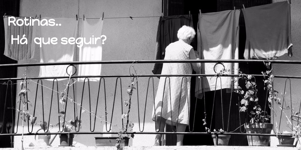 retrato em pb de mulher idosa, de costas, numa varanda com gradil de metal,e estendendo roupas no varal